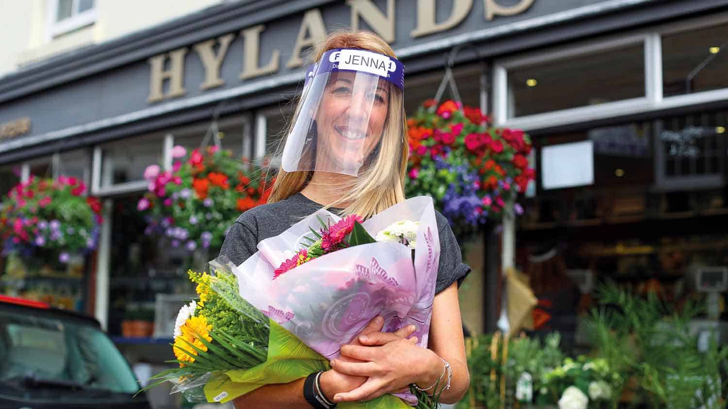 Florist outside her shop, carrying flowers, wearing PPE plastic face mask