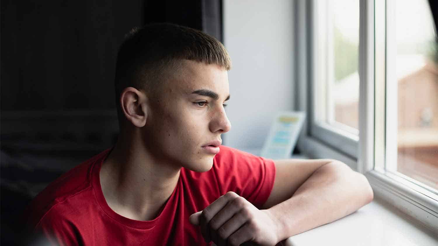 Male teenager looking out of a window