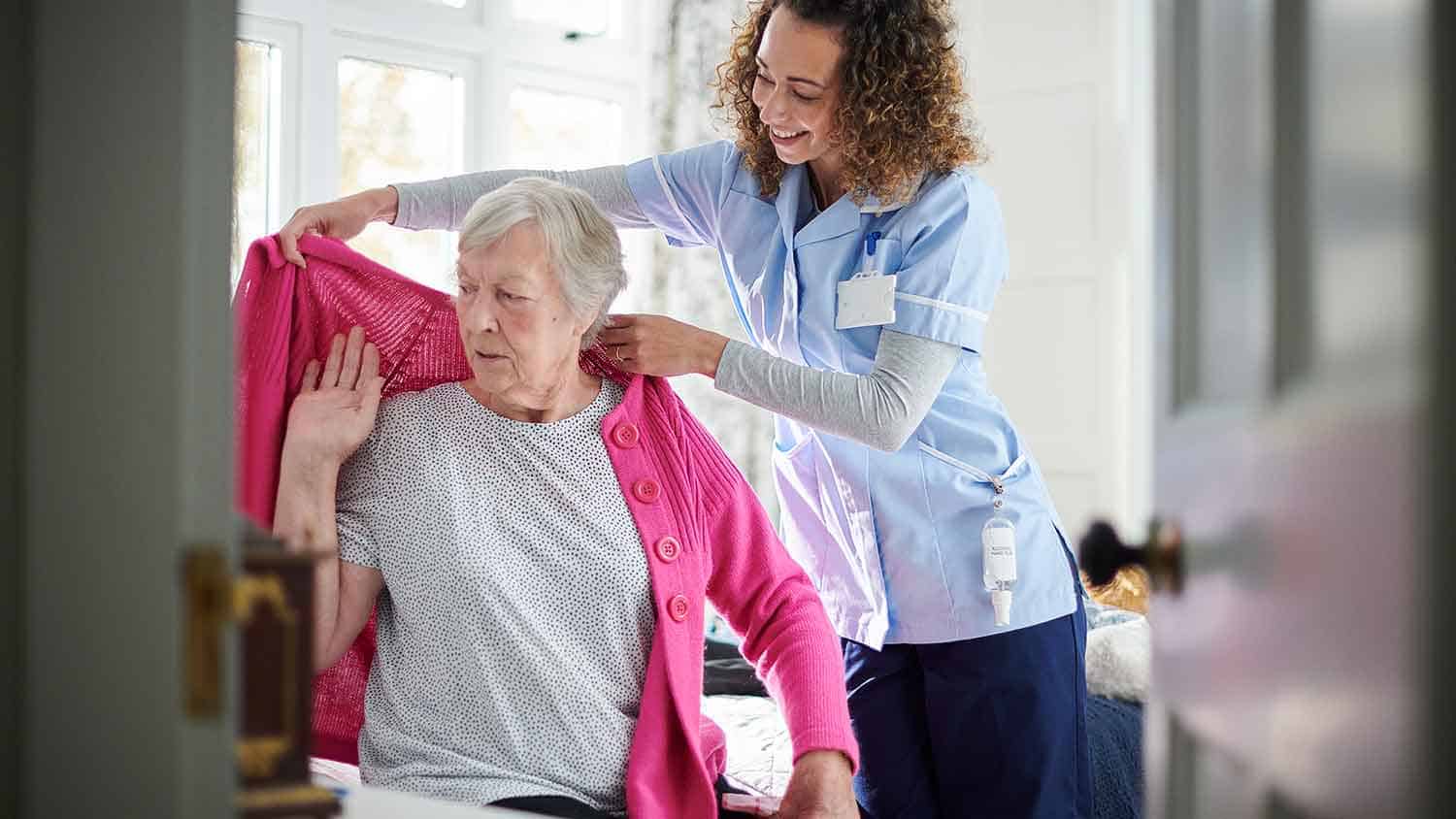 Nurse helping an older lady with a cardigan