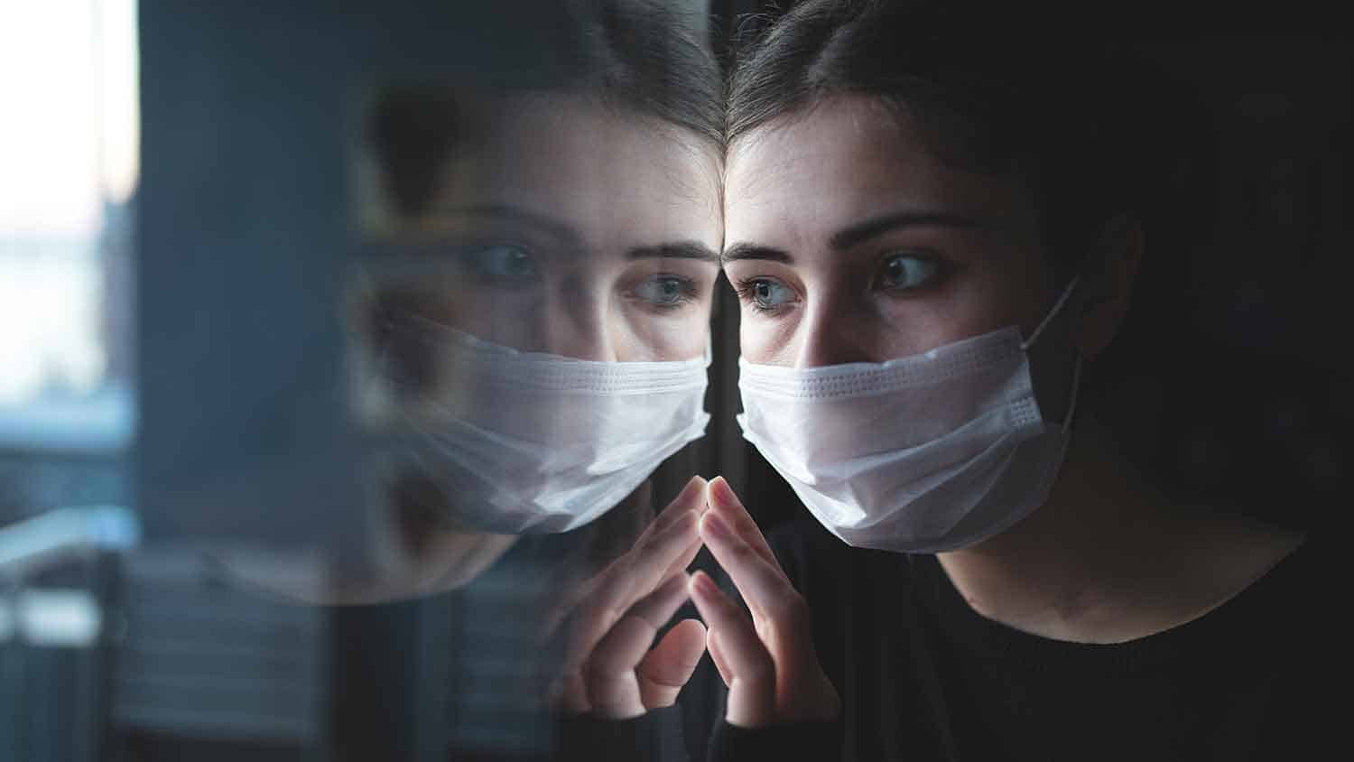 Woman with a mask peering out of a window