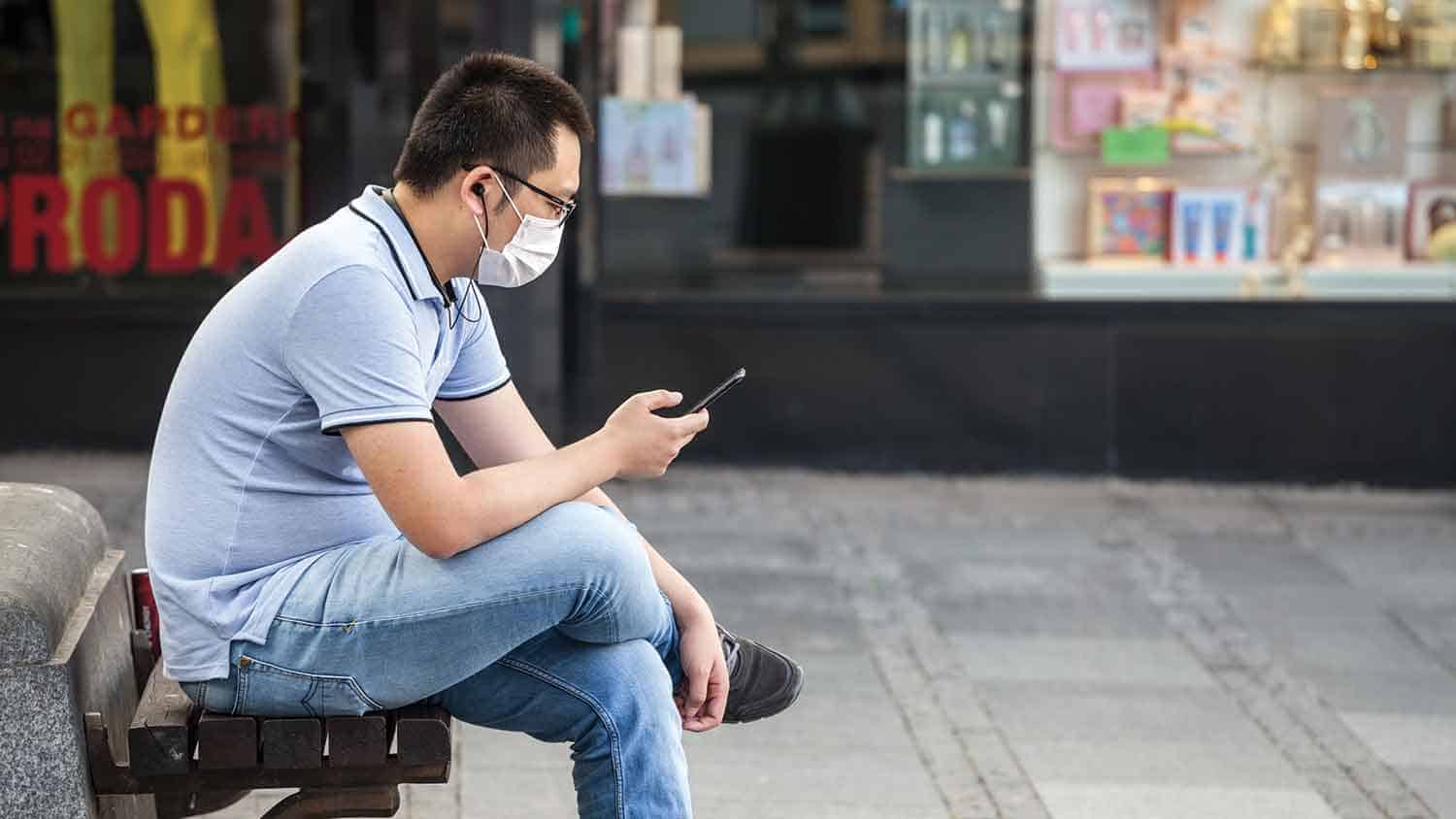 Man sat down wearing a mask and using a mobile phone
