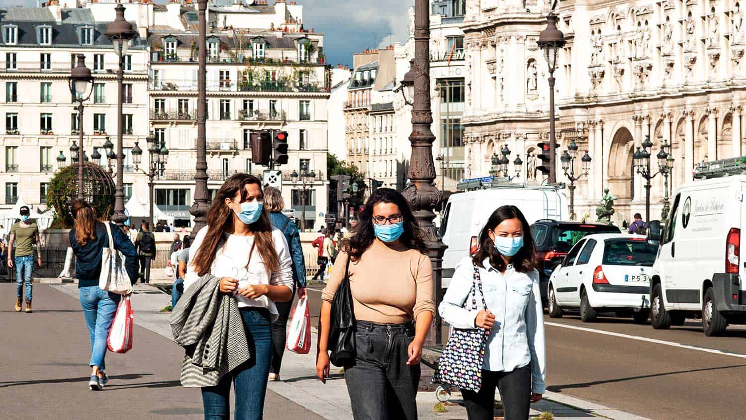 Three women walking down a street all wearing PPE