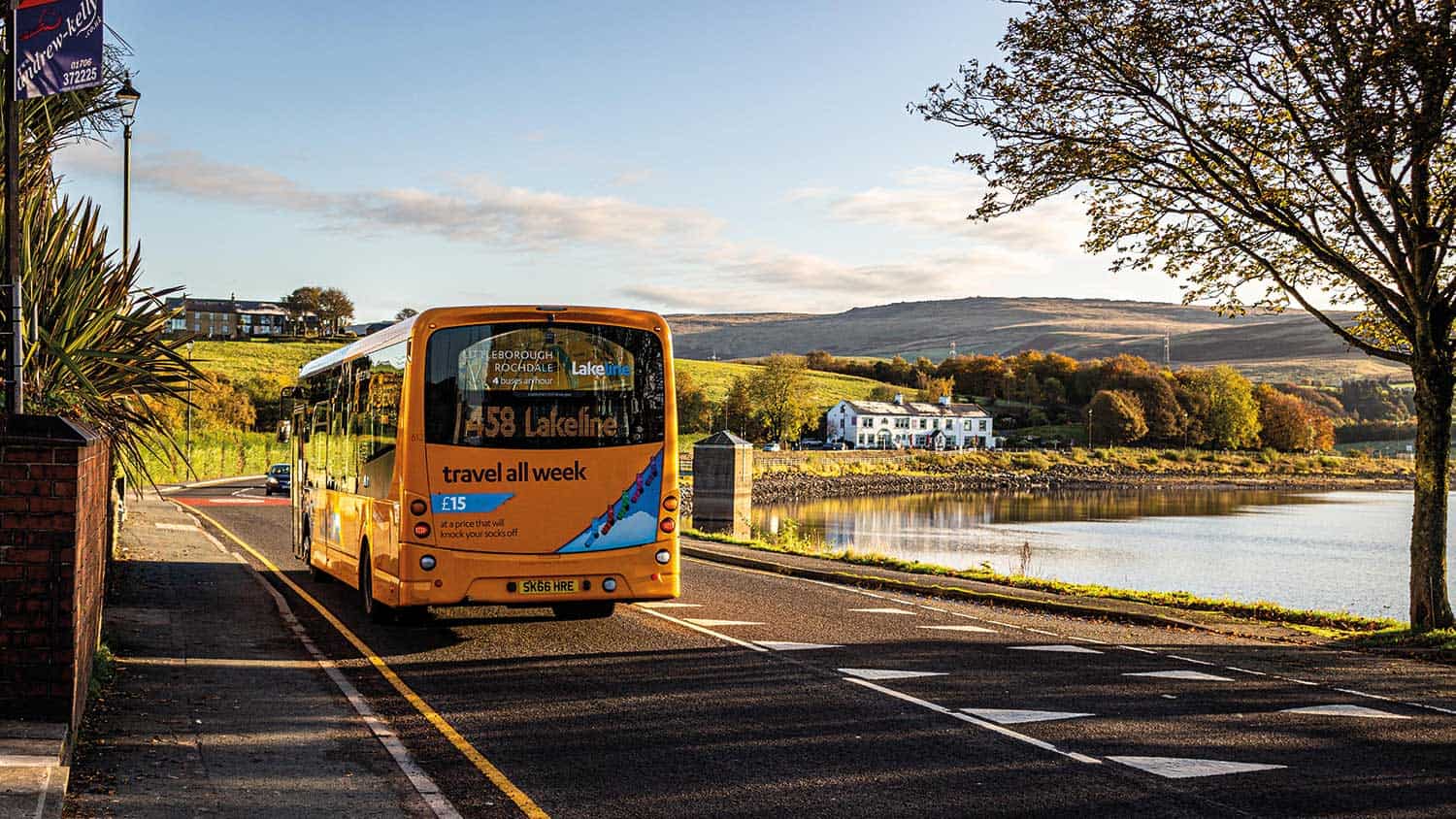 Yellow bus disappearing down the road in rural England with a lake and a village to the side