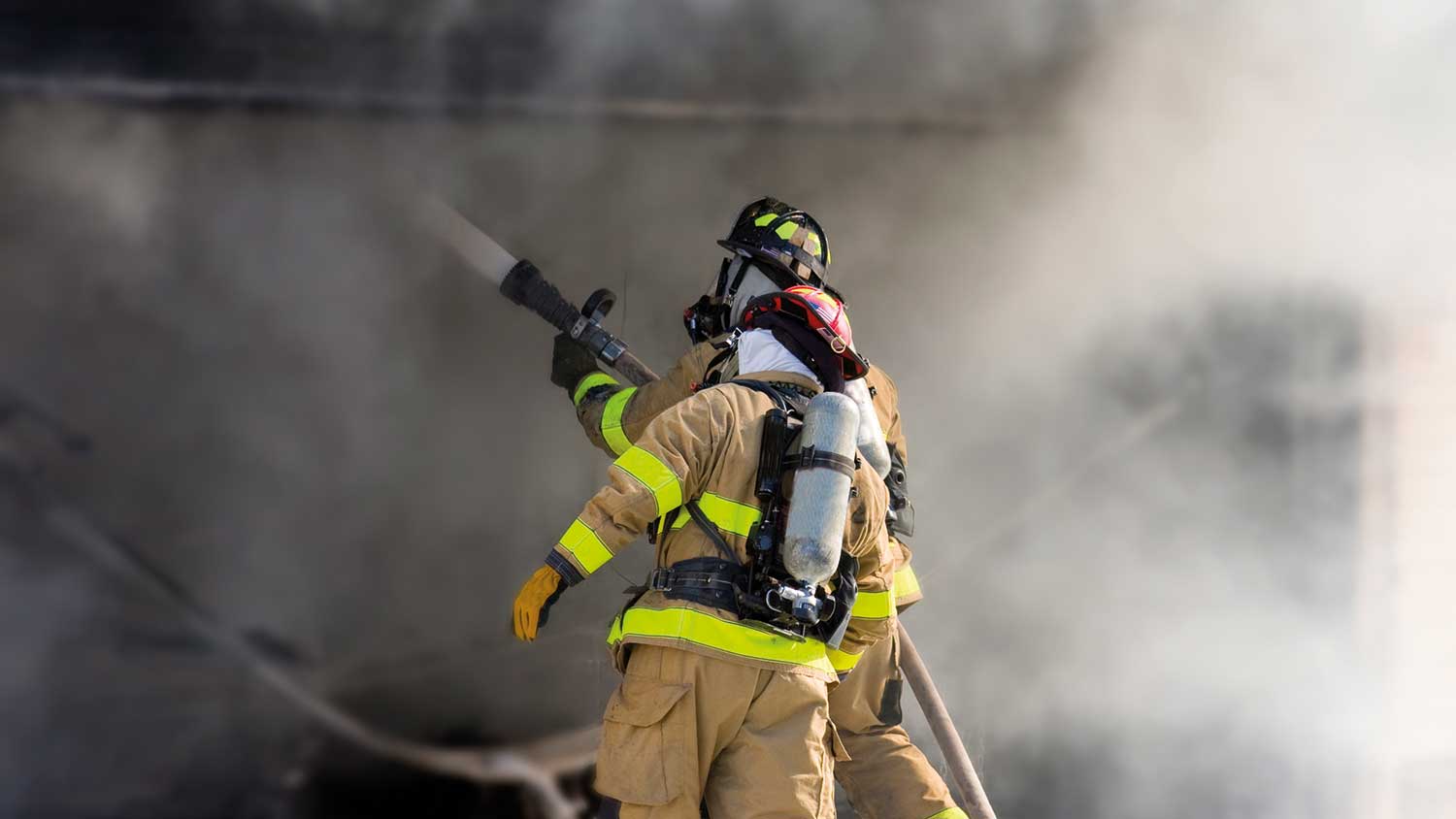 Two firefighters holding the hose and surrounded by smoke