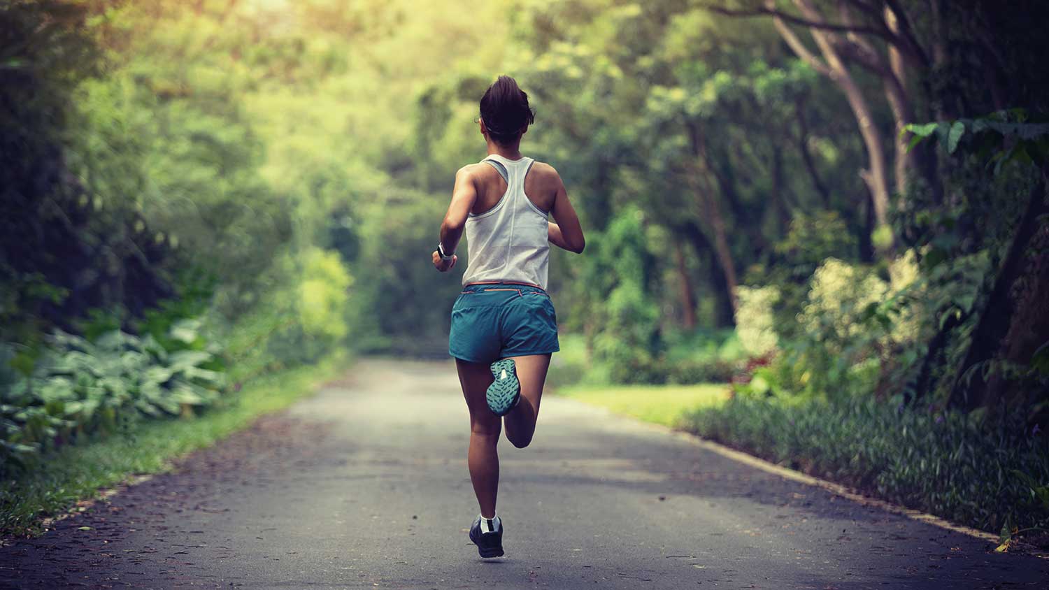 Person running on a road through the woods, the trees are green and lush