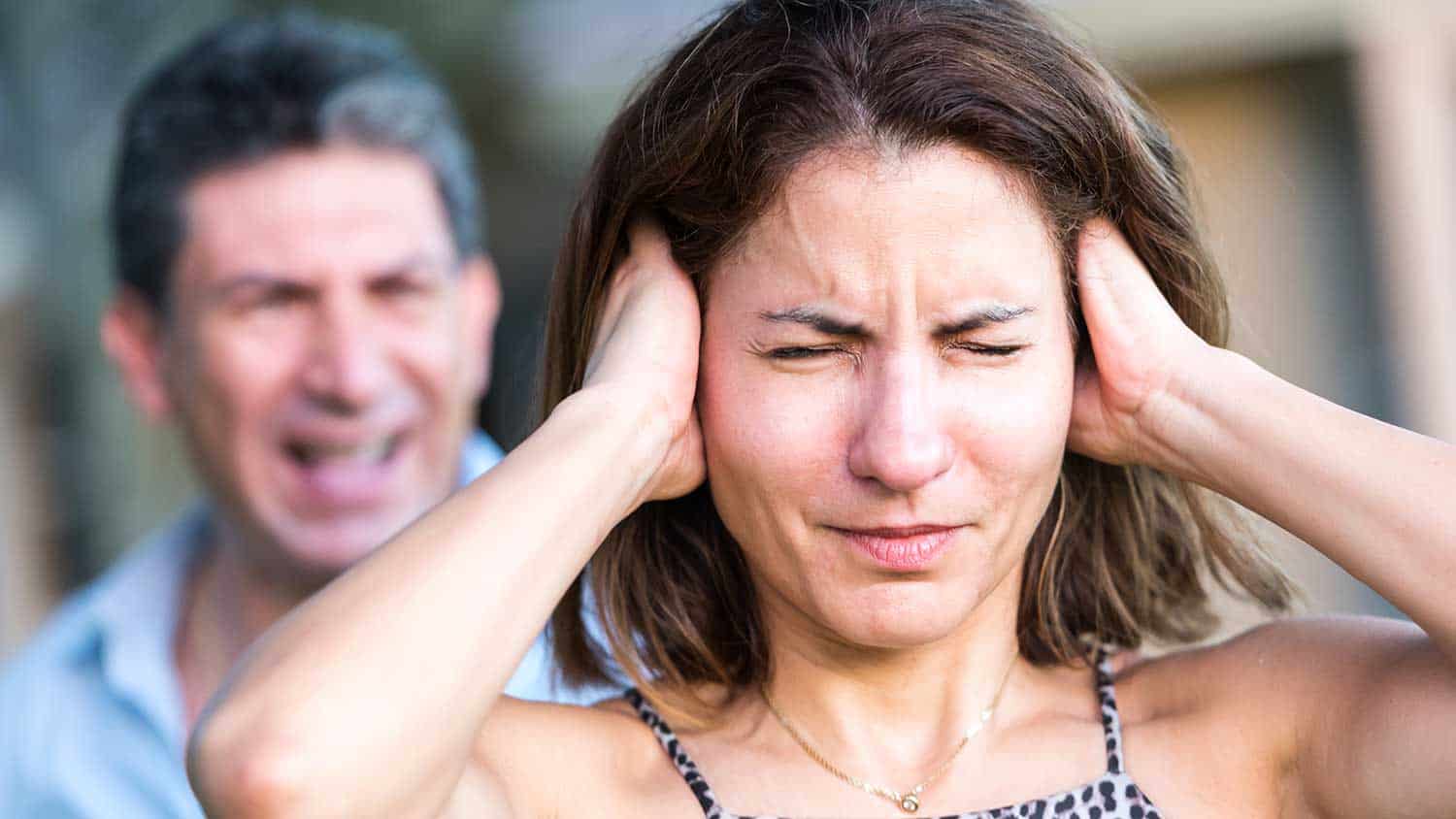 Man shouting at a woman who has her hands over her ears wincing with pain