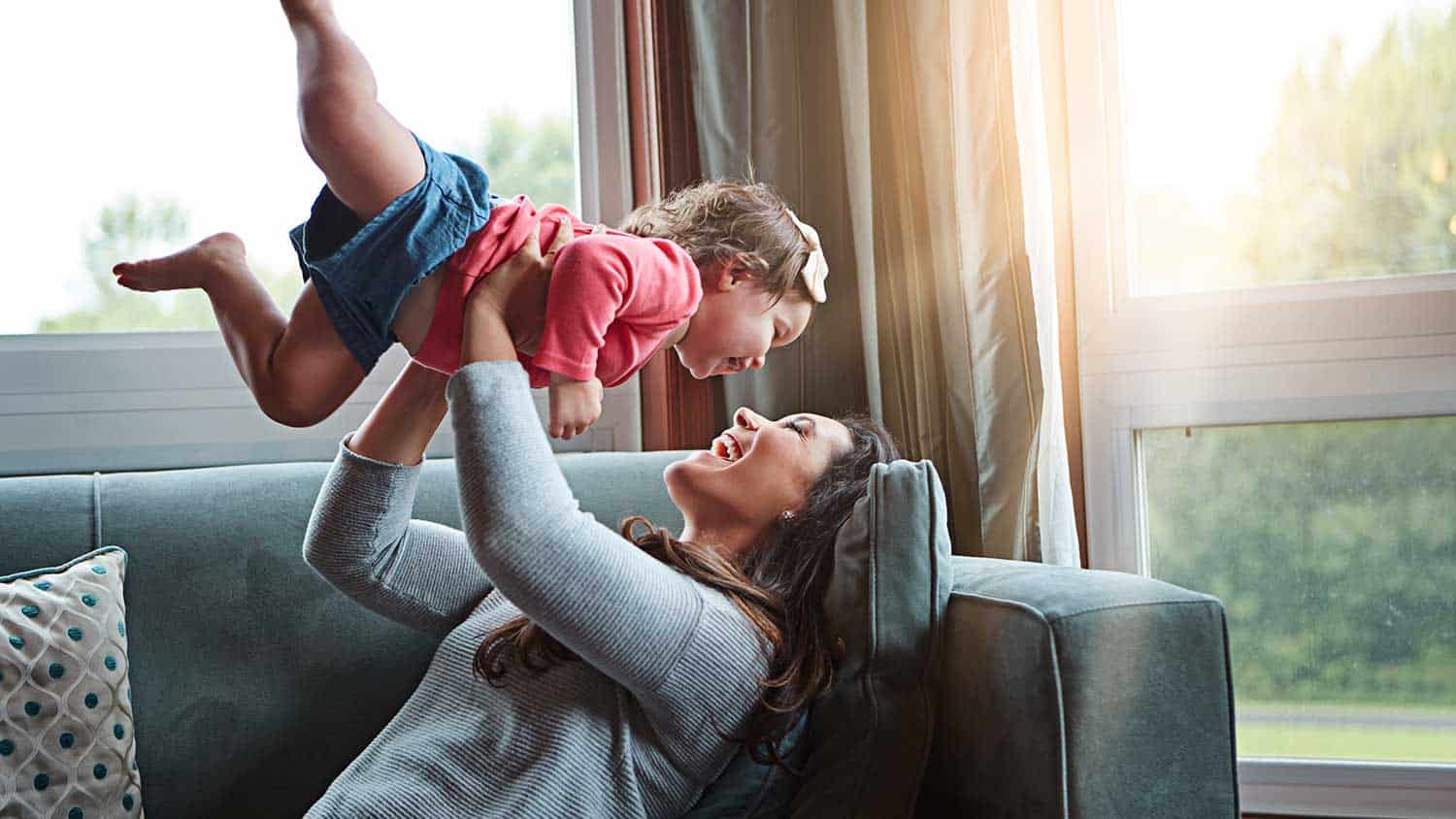 Young mother swinging a little girl on the sofa while playing