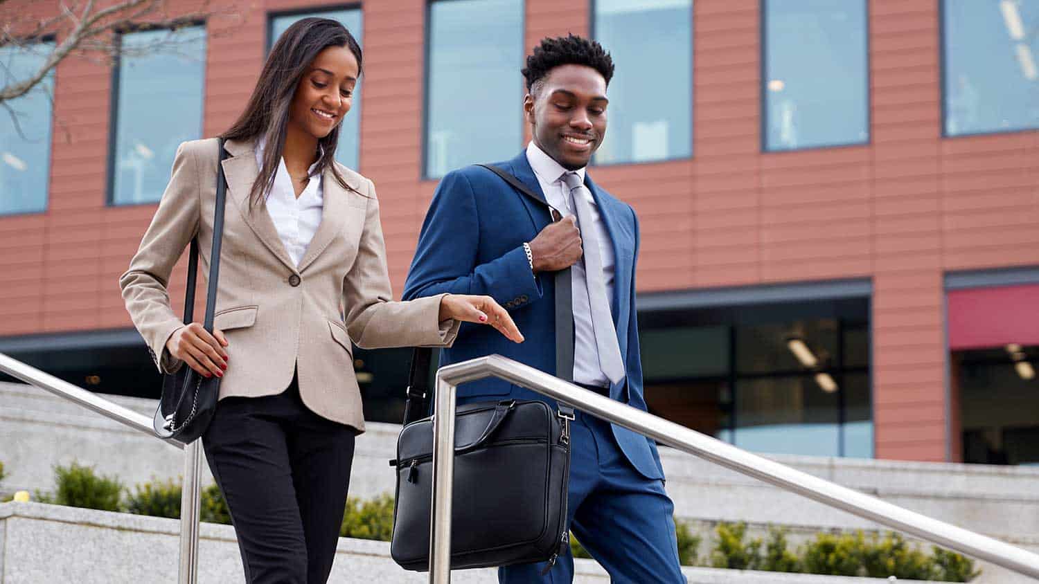 Two young professionals walking down a set of stairs while talking to each other