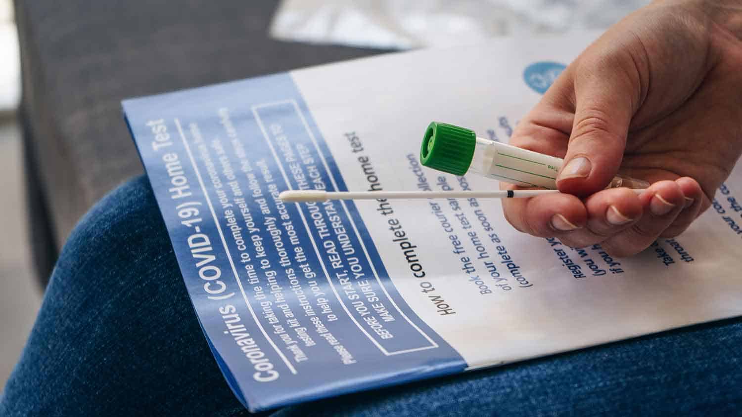 A hand holding a COVID test swab and tube