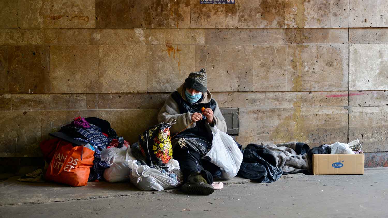 A homeless person sitting on a street surrounded by belongings