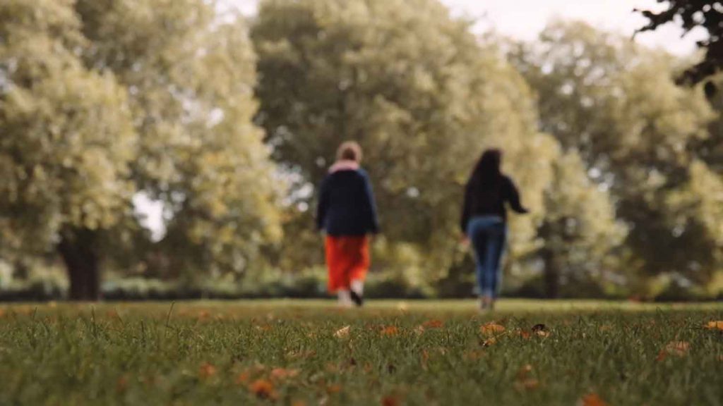 Two women walking in a leafy park away from the camera, they are slightly out of focus