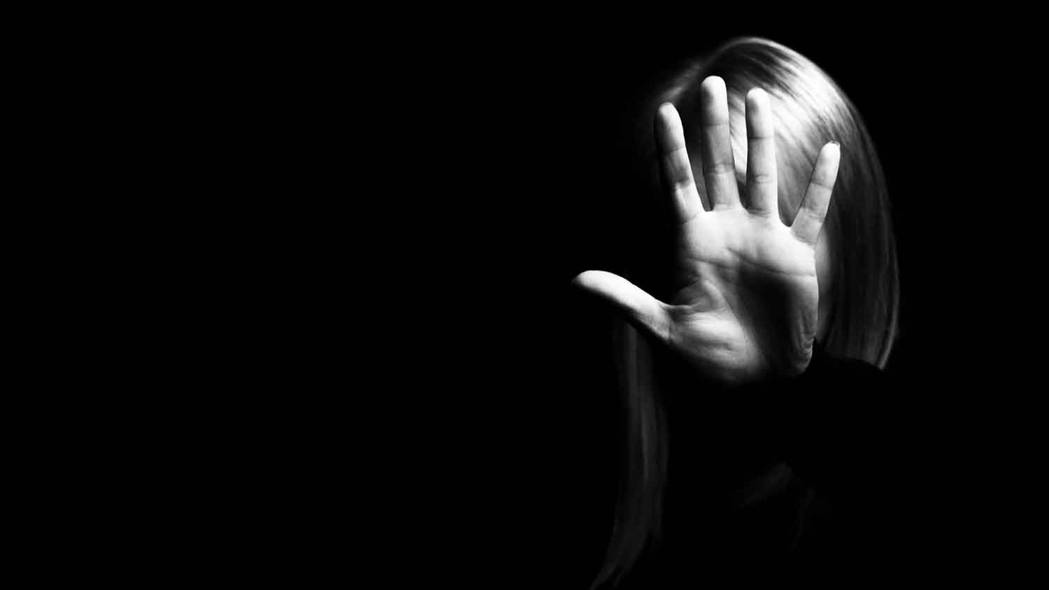 Black and white image of a woman holding her hand toward the camera to obscure her face