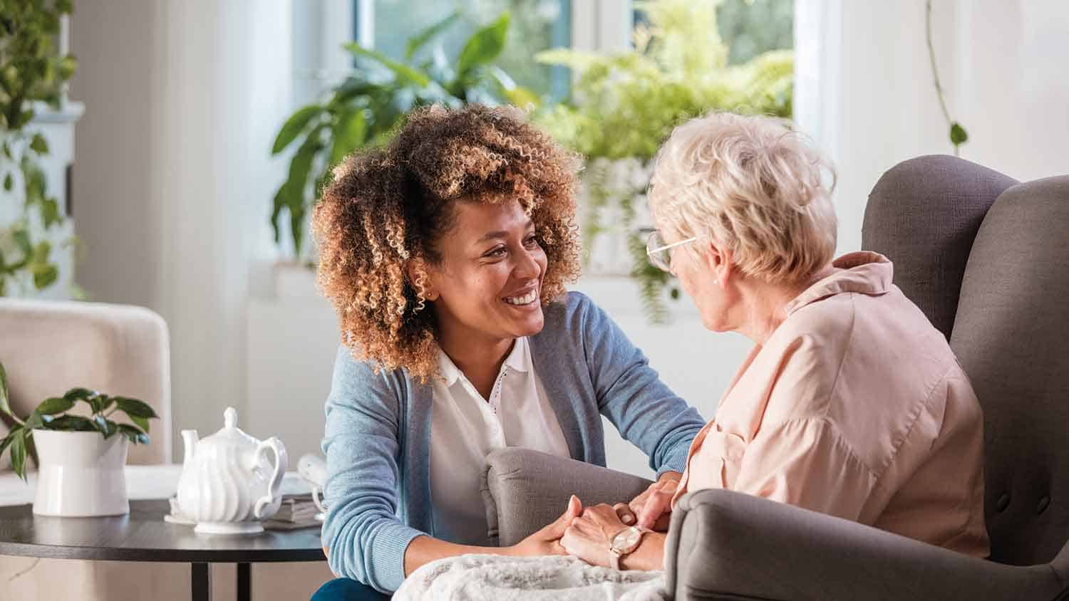 A carer holding on to an older woman's hands and smiling