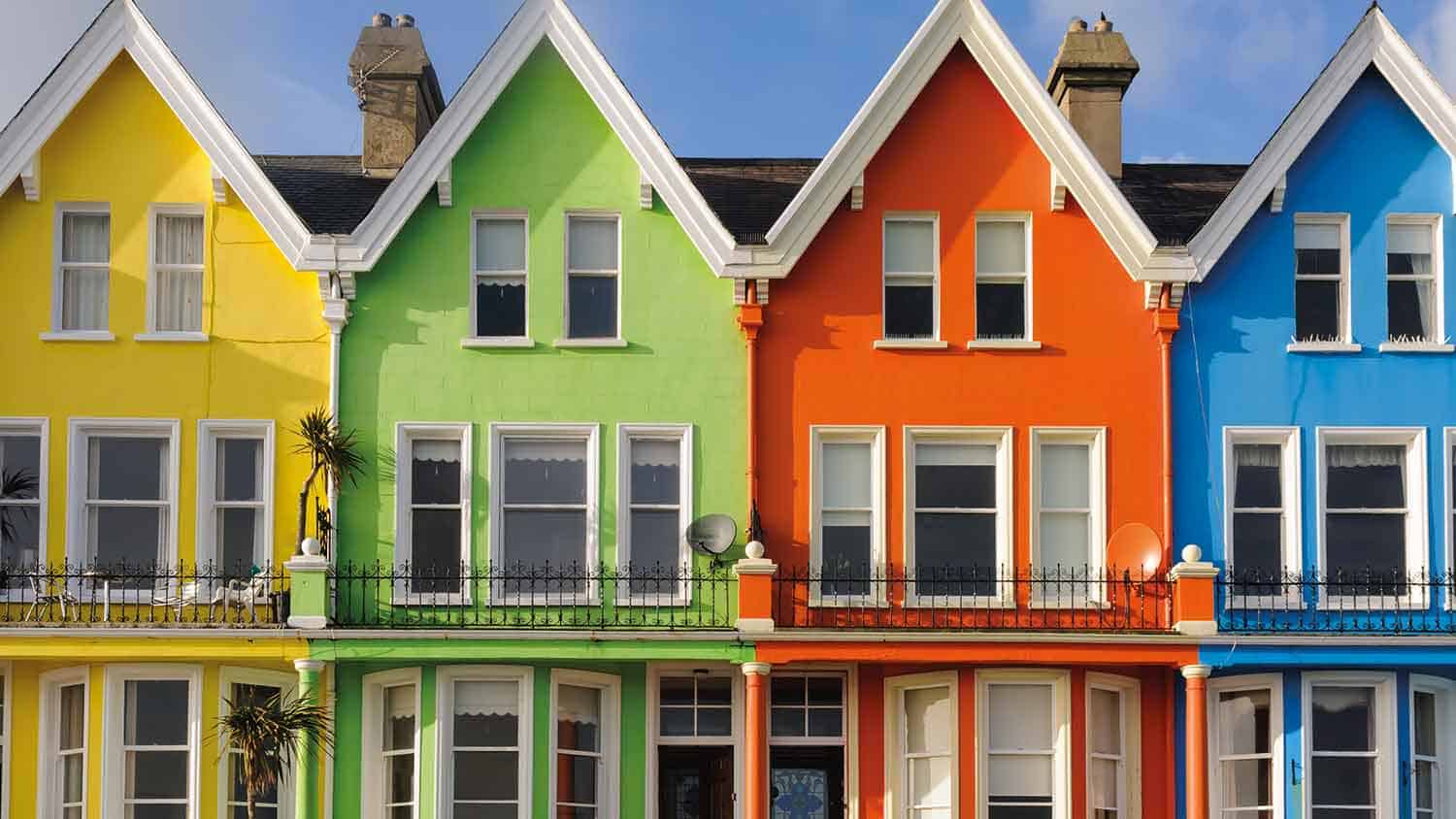 Row of houses painted in bright colours. From left to right they are yellow, green, orange and blue. All against a sunny blue sky