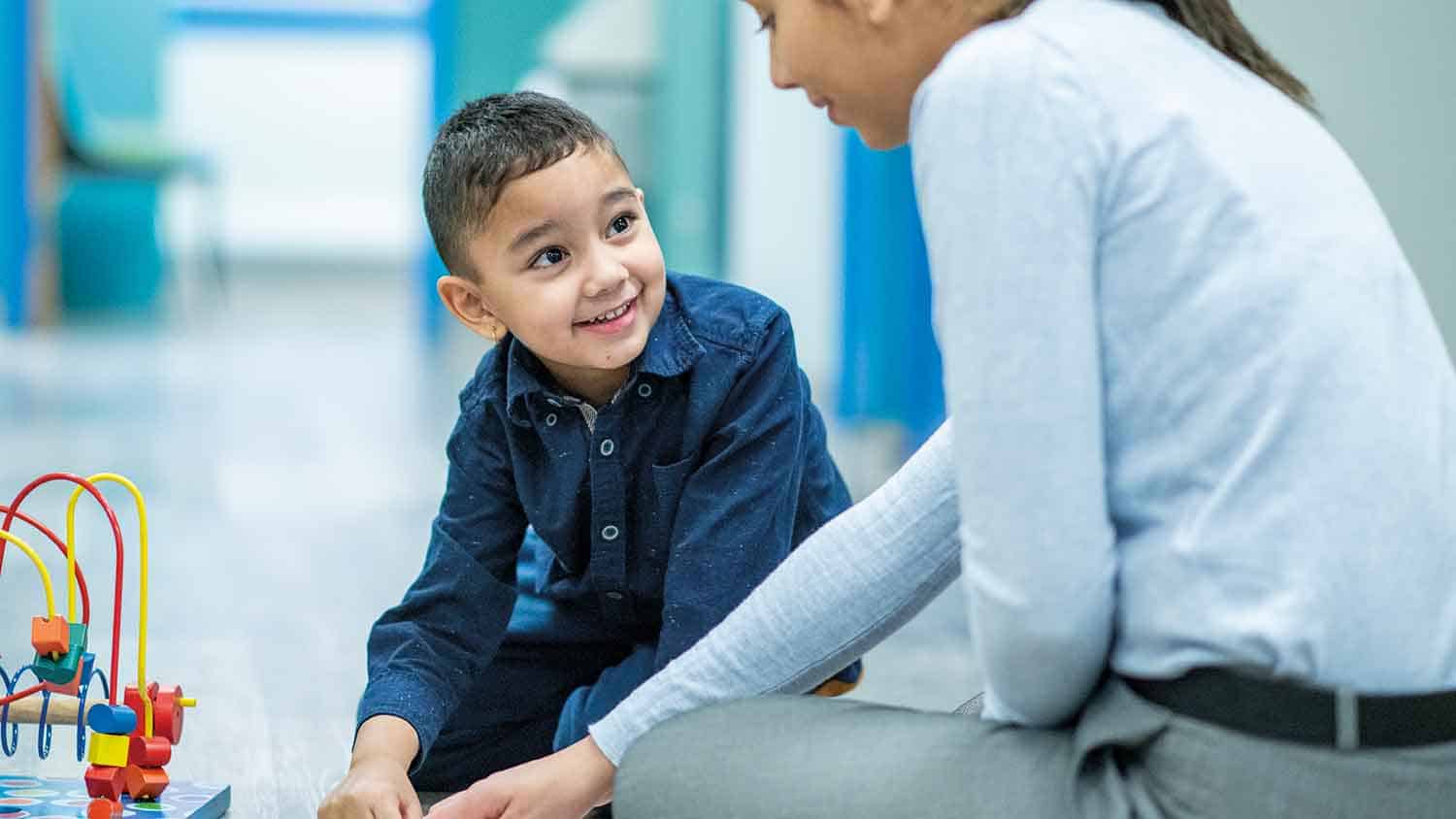 Young boy of about 5 years old smiling at a woman whilst playing with toys