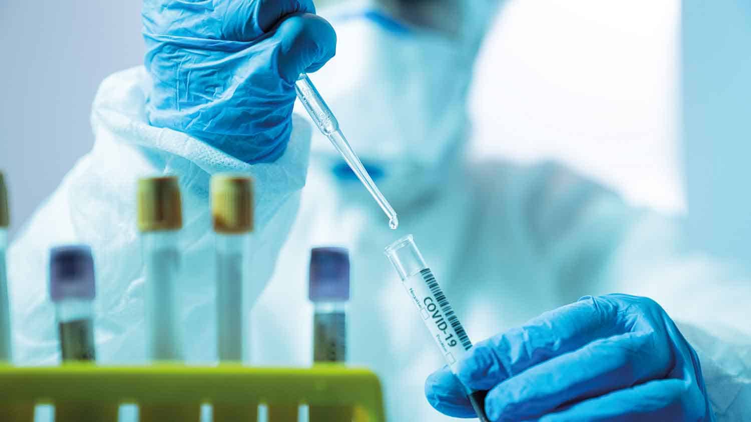 Scientist pipetting a liquid into a vial labelled COVID-19