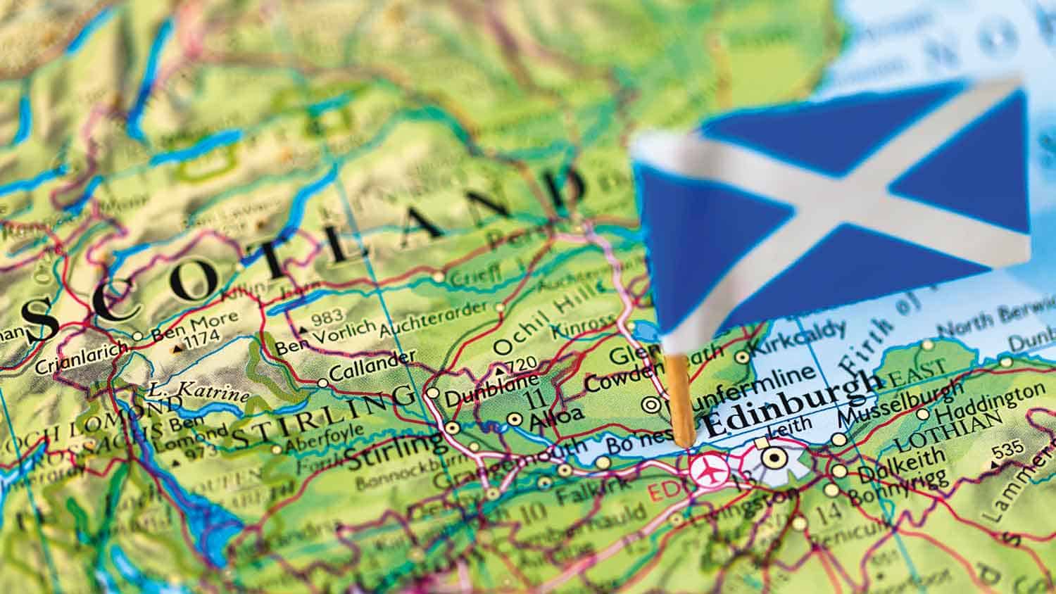 Scotland flag on a small wooden stick poked into Edinburgh on a map of Scotland