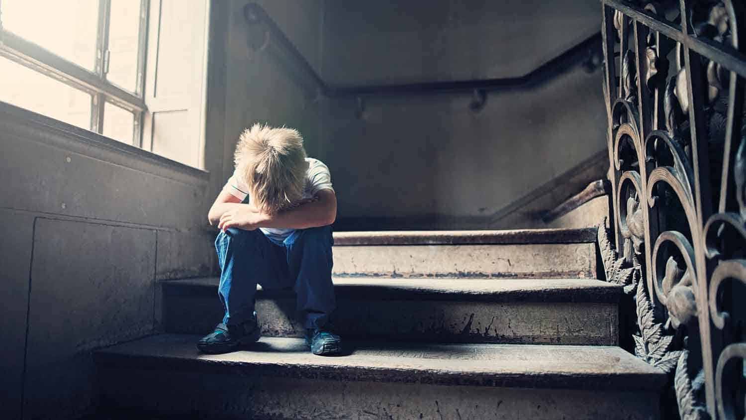 Small boy crying on the stairs, head in hands