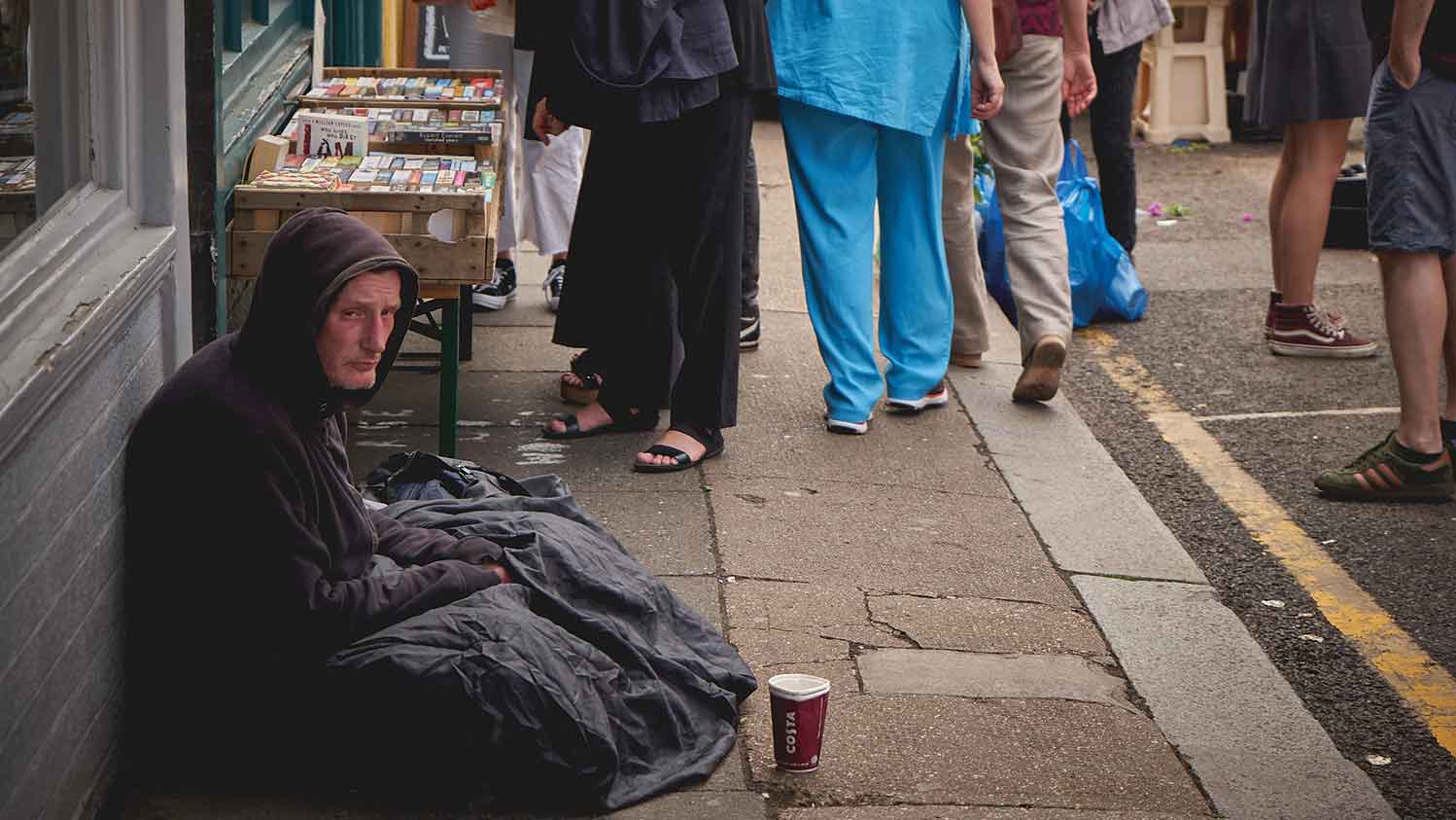 Homeless man sat on the pavement with a coffee cup for money in front of him