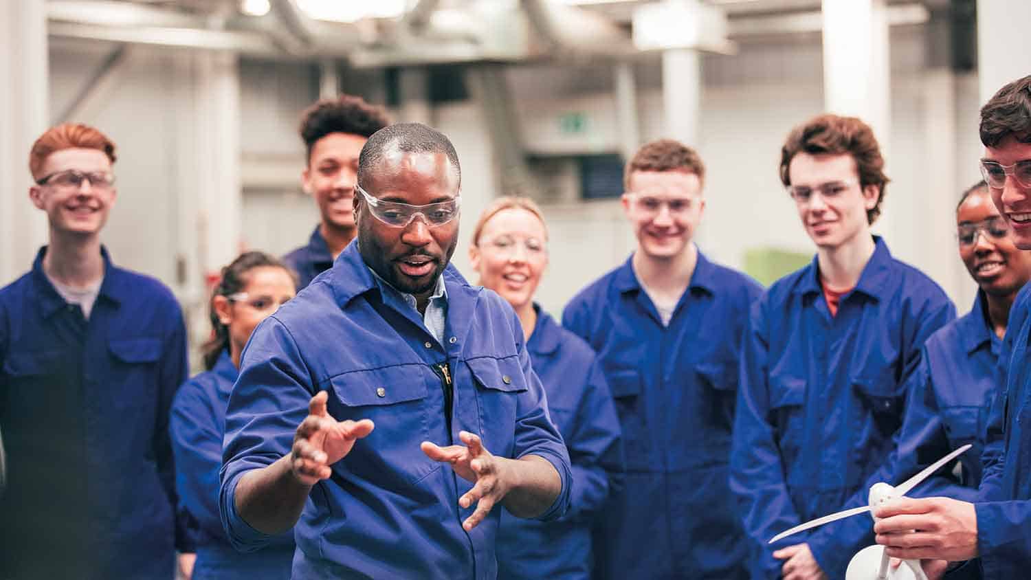 Group of apprentice mechanics listening to a teacher and smiling