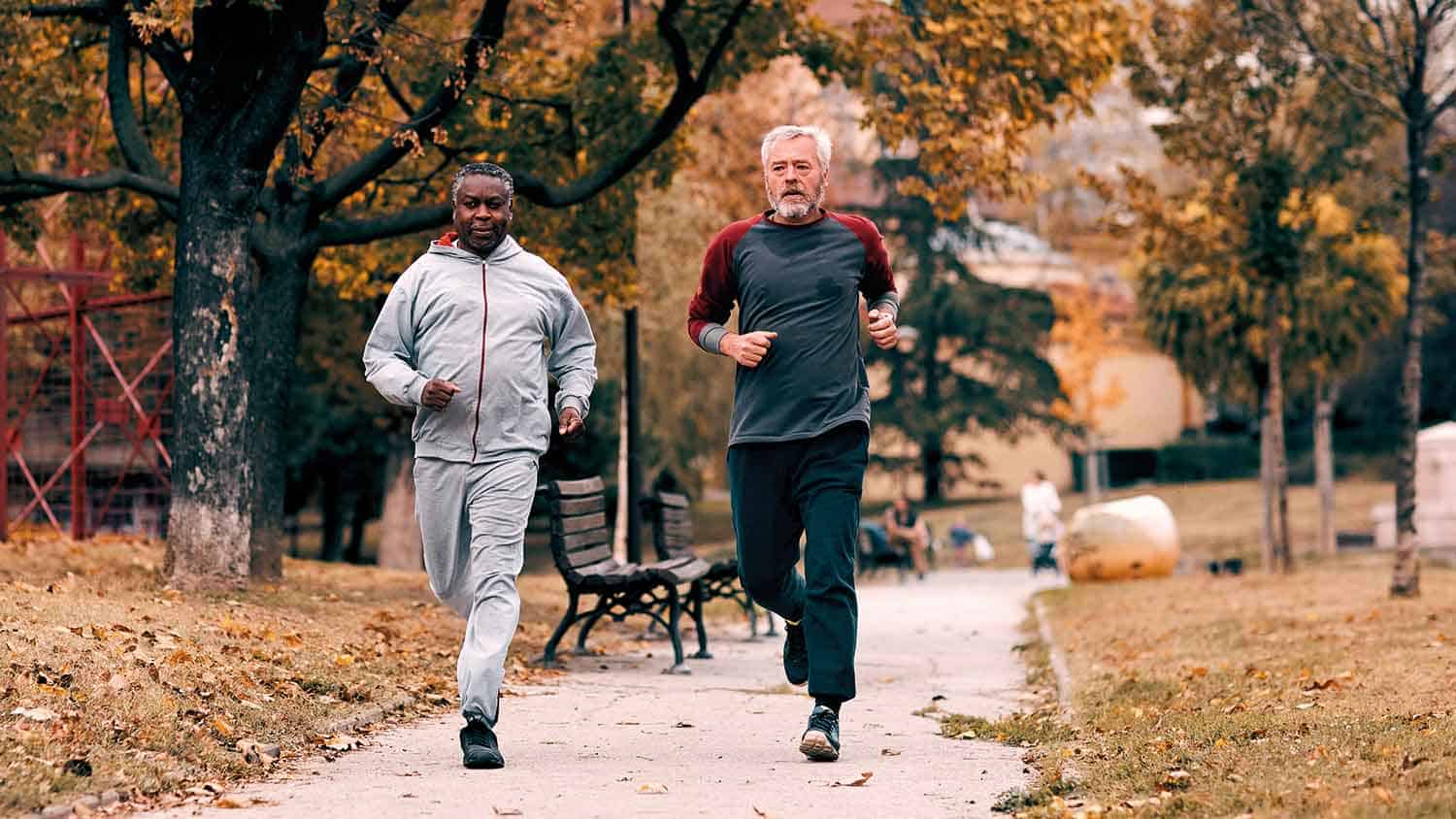 Two older men jogging through a park in early autumn