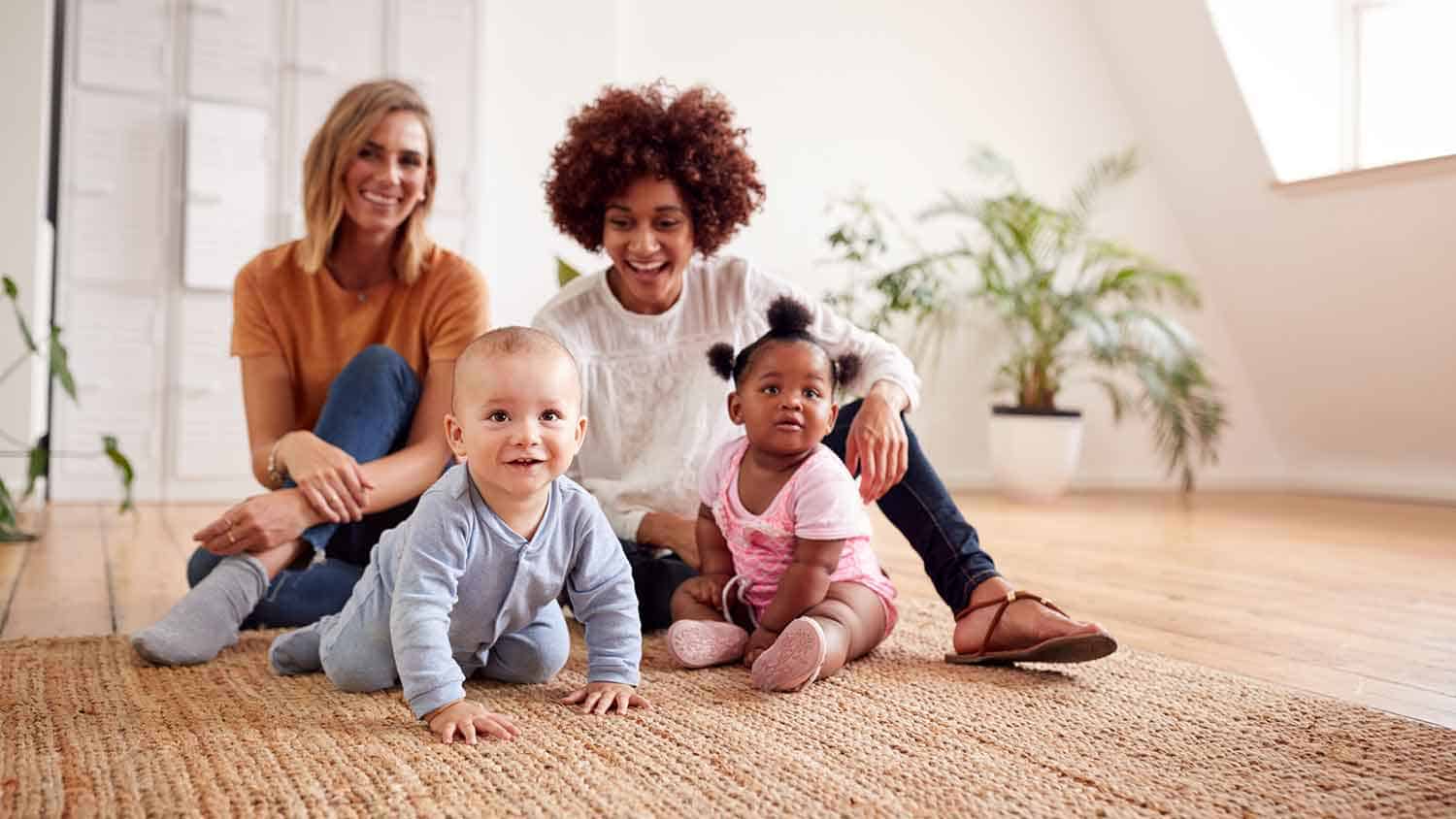 Two women sat on the floor with their young babies crawling toward the camera.