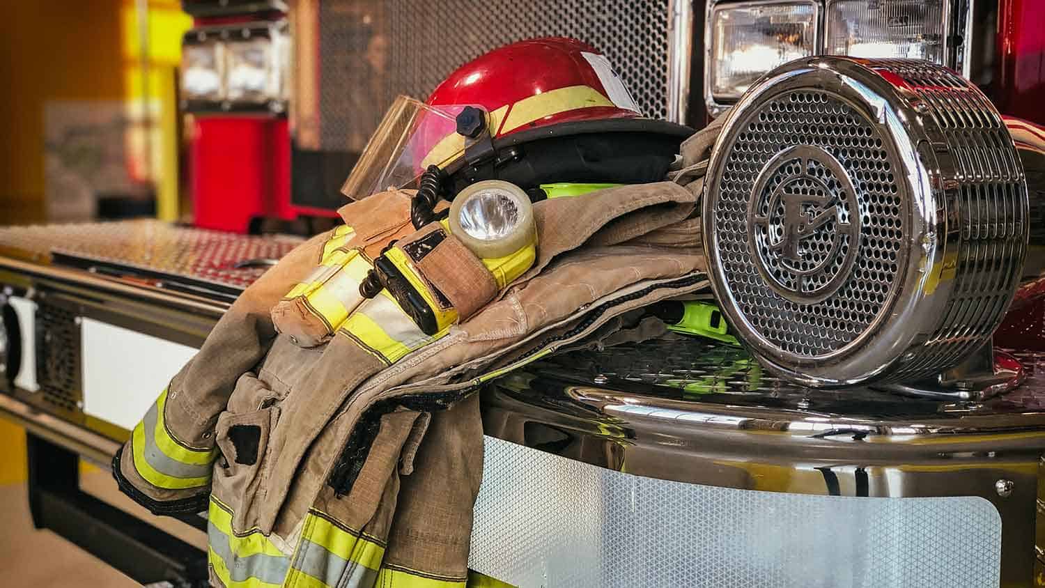 Fire mans uniform resting on the side of a fire engine, hat placed on top of jacket