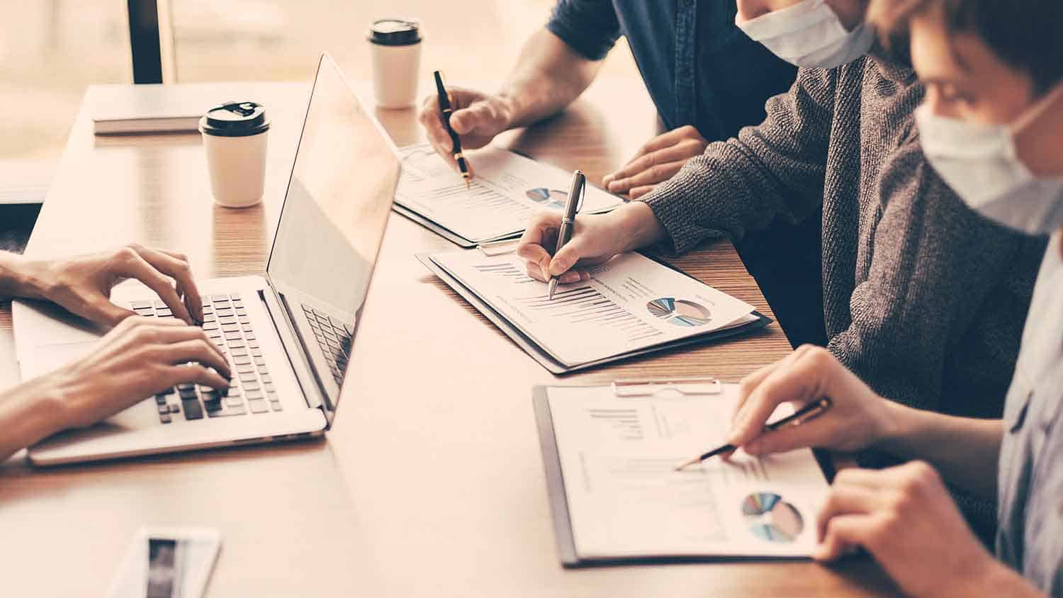 Four people working on documents, each marking things on a graph in front of them.