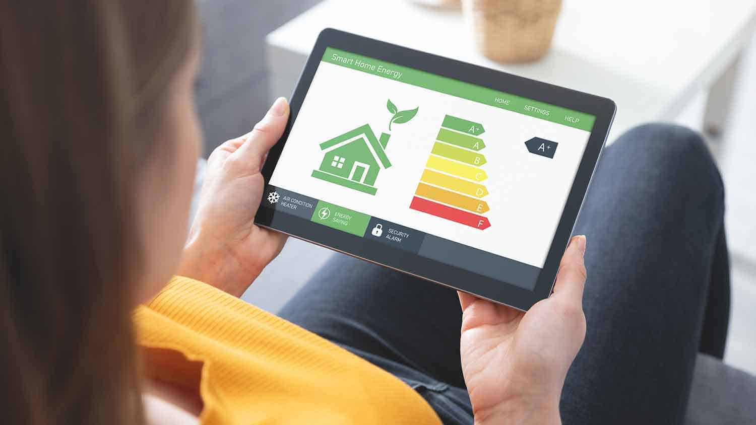 Woman looking at a computer tablet with 'smart home energy' readings on it. He rating is A+