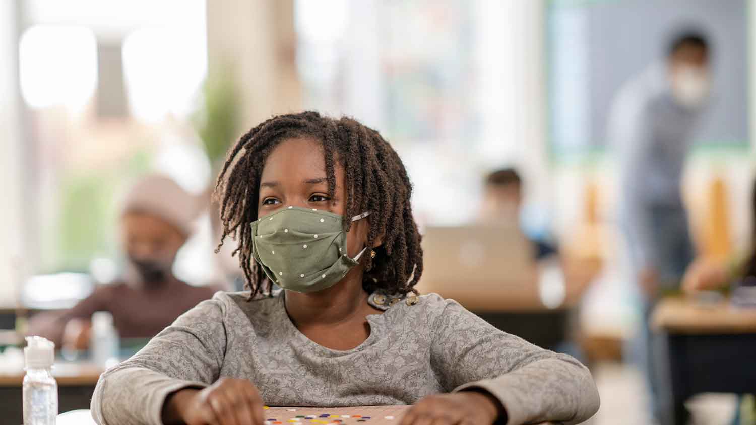 Young school age child wearing a cloth PPE mask listening to someone talking