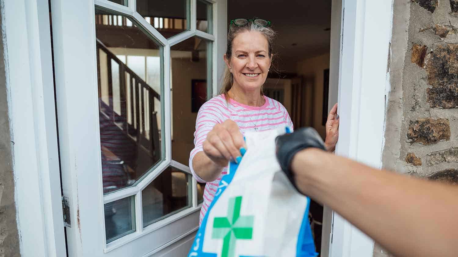 Delivery of a pharmacy prescription to a door opened by a middle aged woman grateful to receive