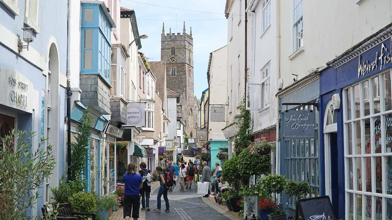 Old market town side street with quaint small shops and cobbled pavement. A church tower can be seen at the end of the street.