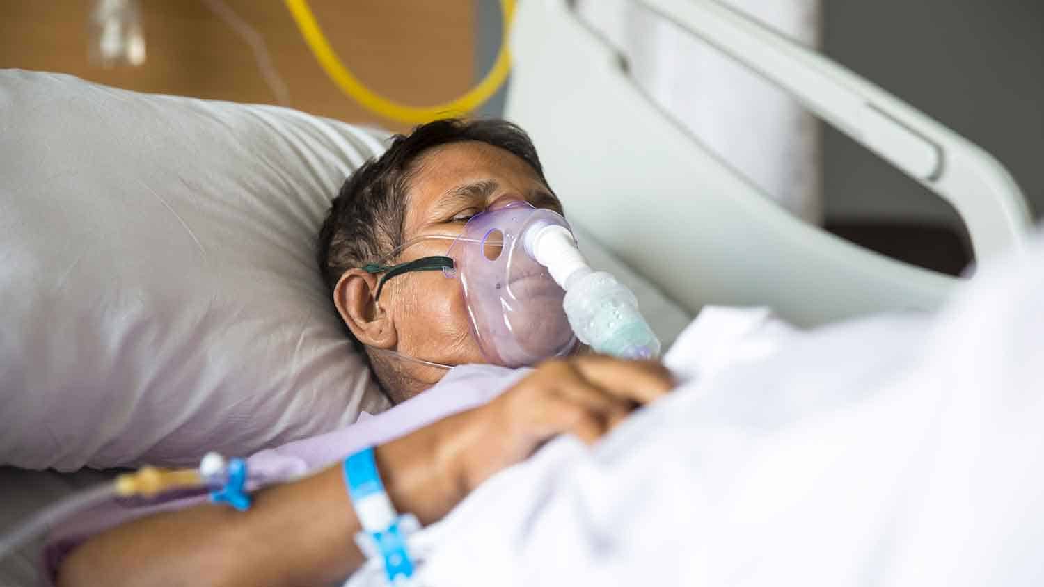 Man in hospital bed with an oxygen mask strapped over his face.