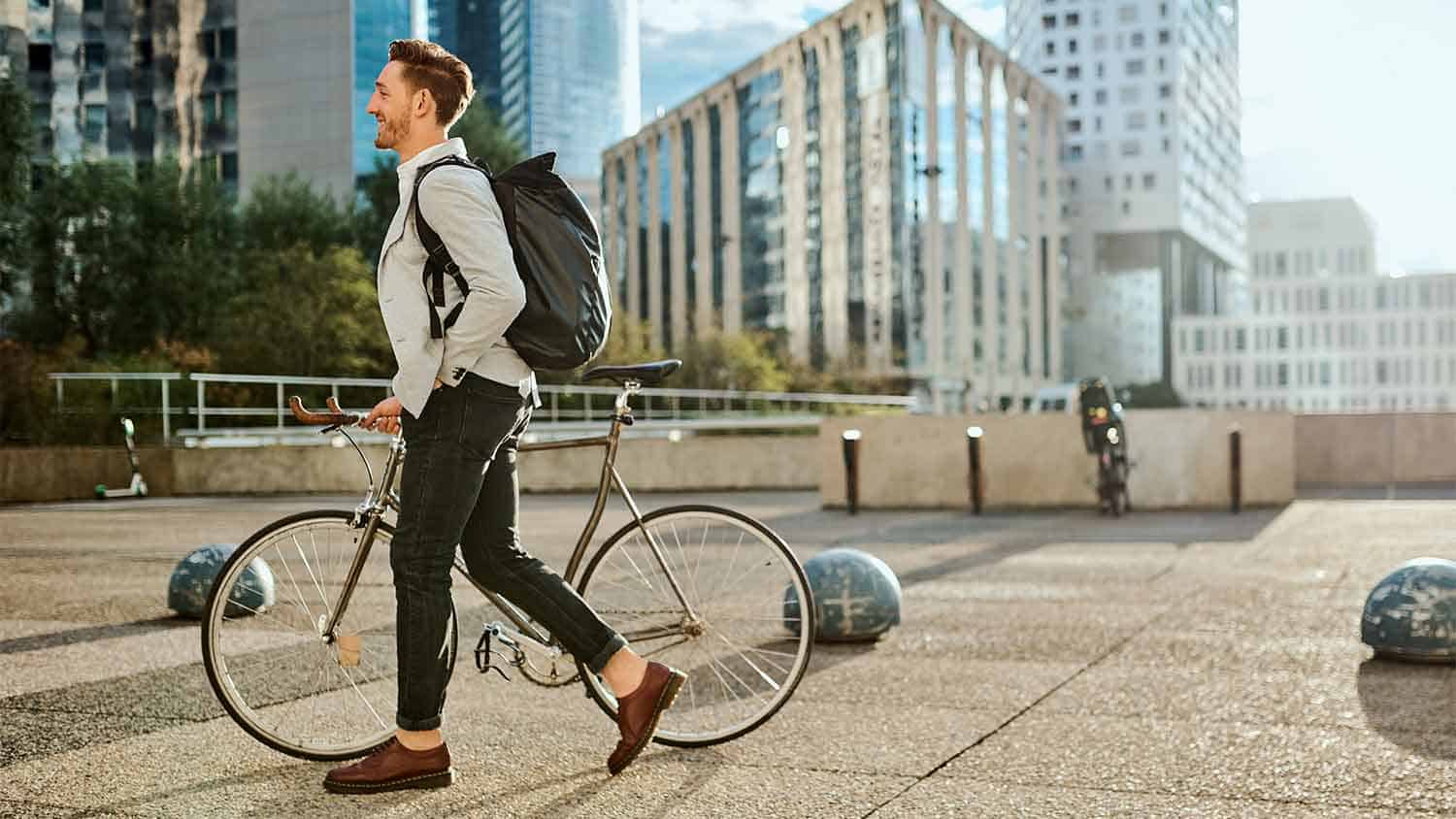 Man pushing a bike across paved area of the city