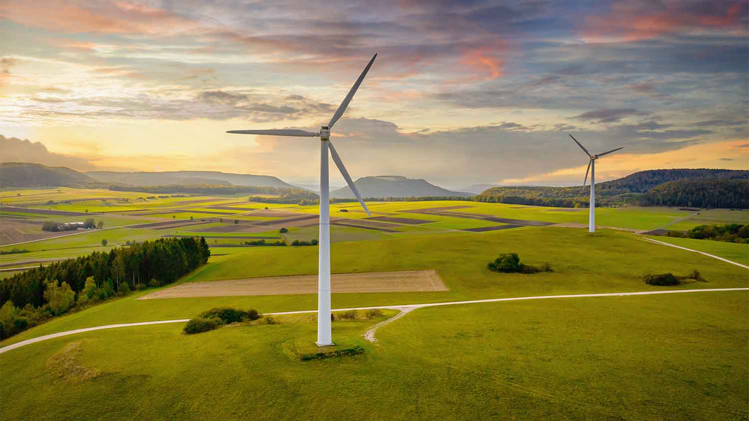 Wind turbines in green rolling countryside. The sun is setting in the background.