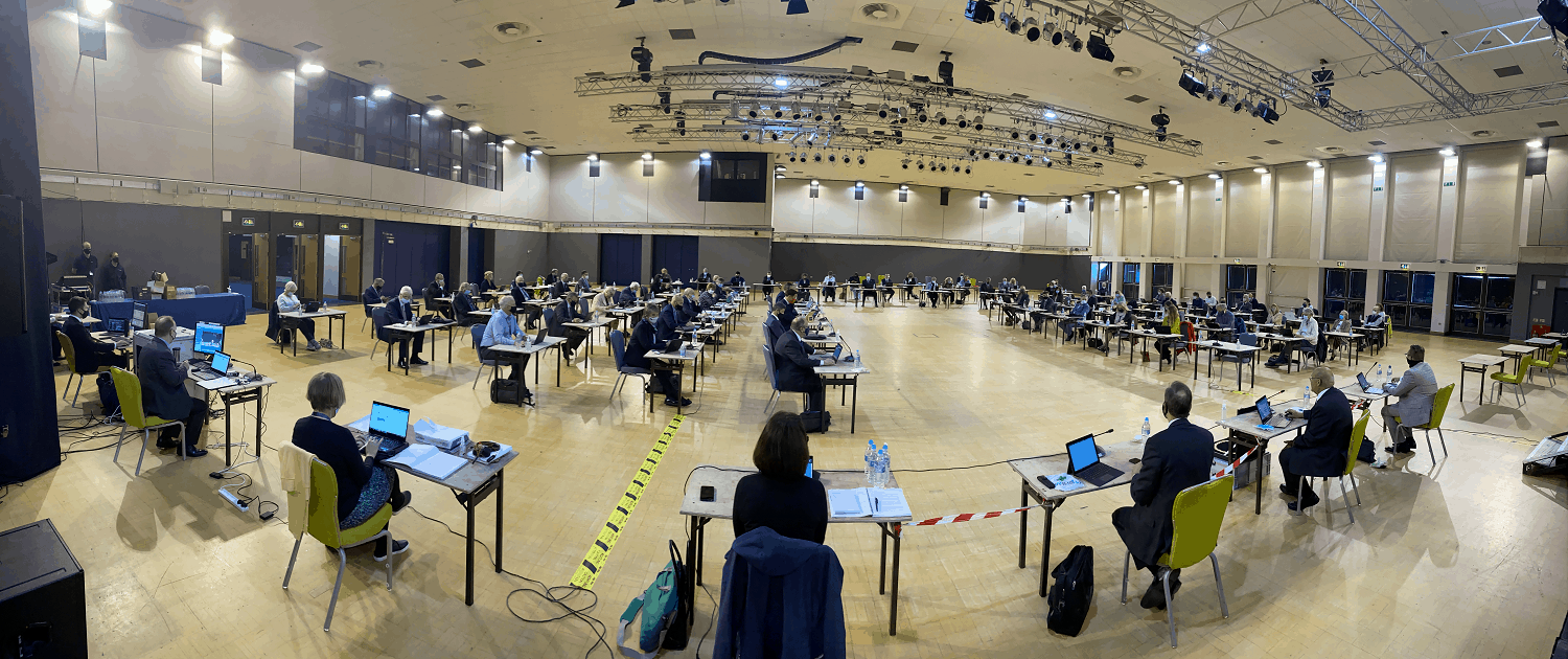 Council members sitting socially distanced in a large hall