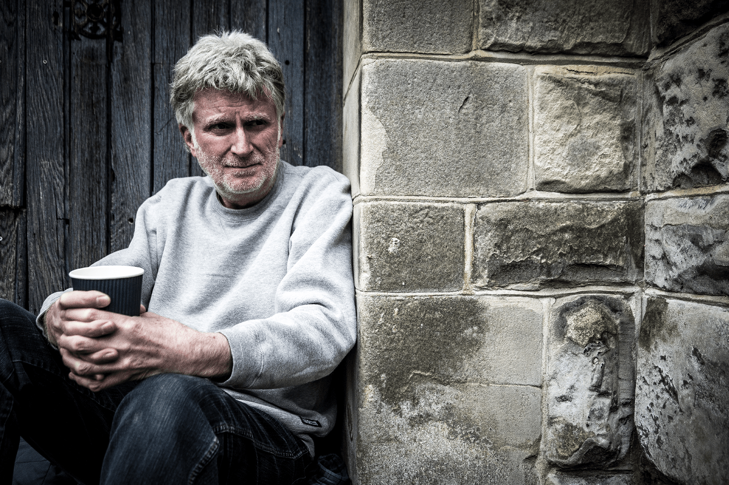 A homeless man crouched by a brick wall