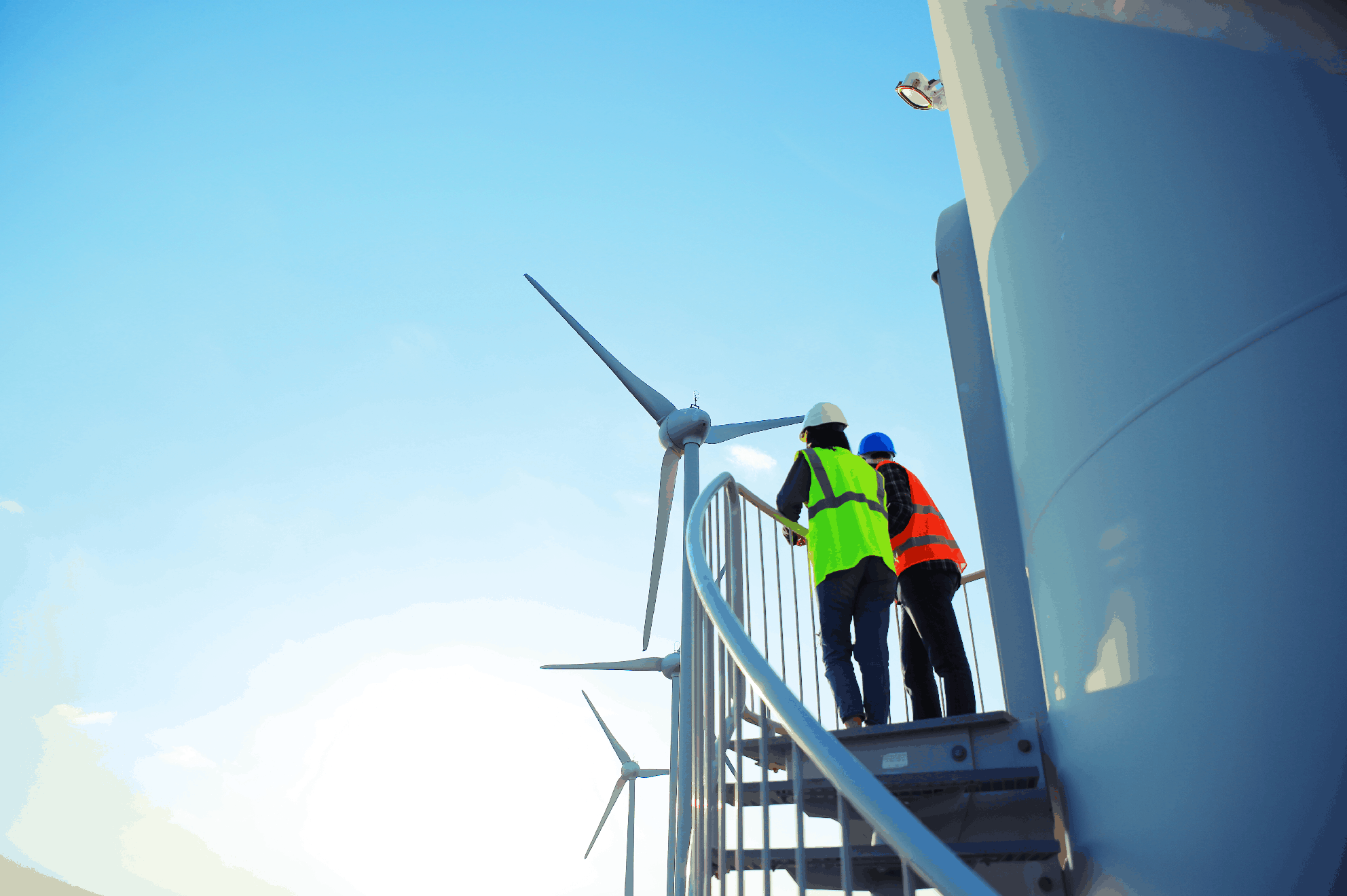 Two construction workers standing in a field of wind turbines