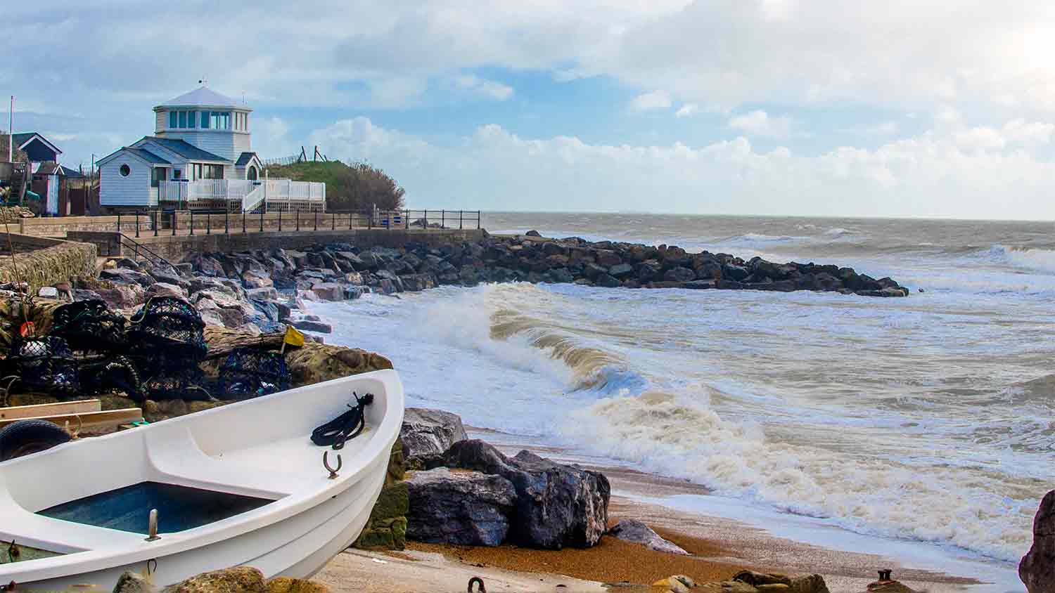 A bay with rough sea waves crashing down. A white dinghy is pointing out to sea but is safely on land