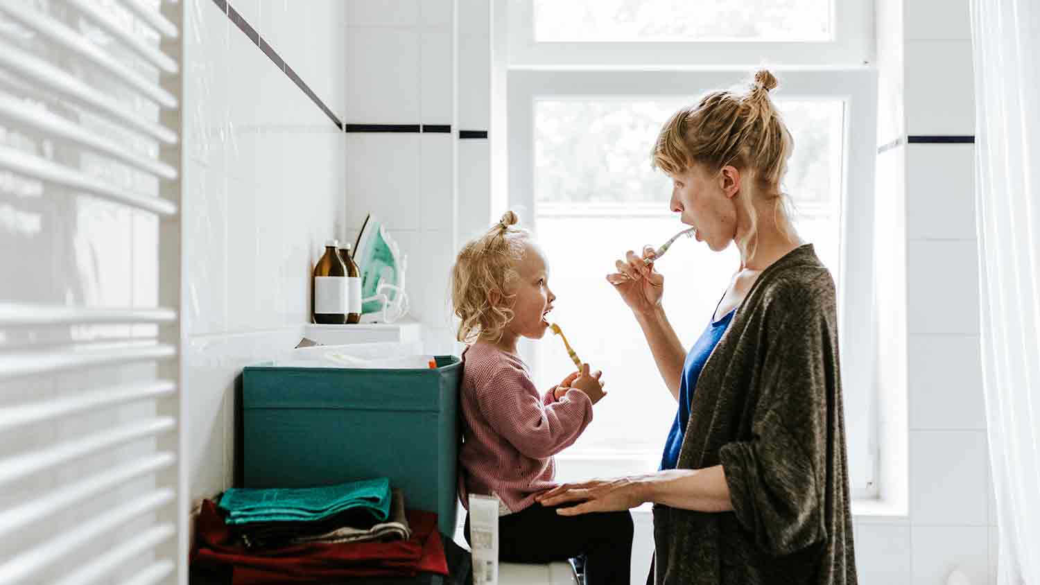 Toddler and mother face each other both brushing their teeth