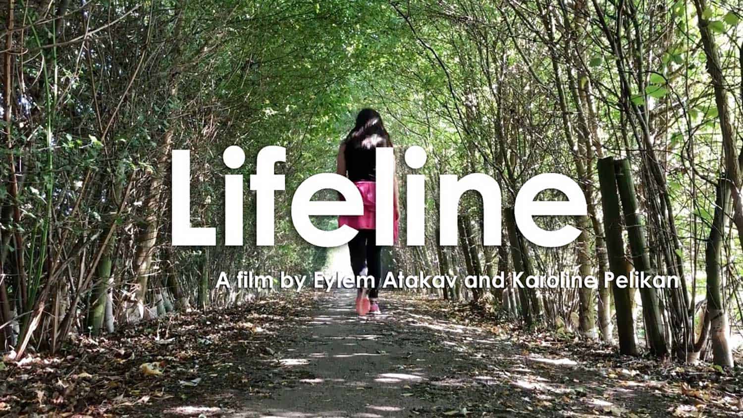 Lifeline - a film by Eylem Atakav and Karoline Pelikan. A woman in the background walks through a forest dappled with sunshine.