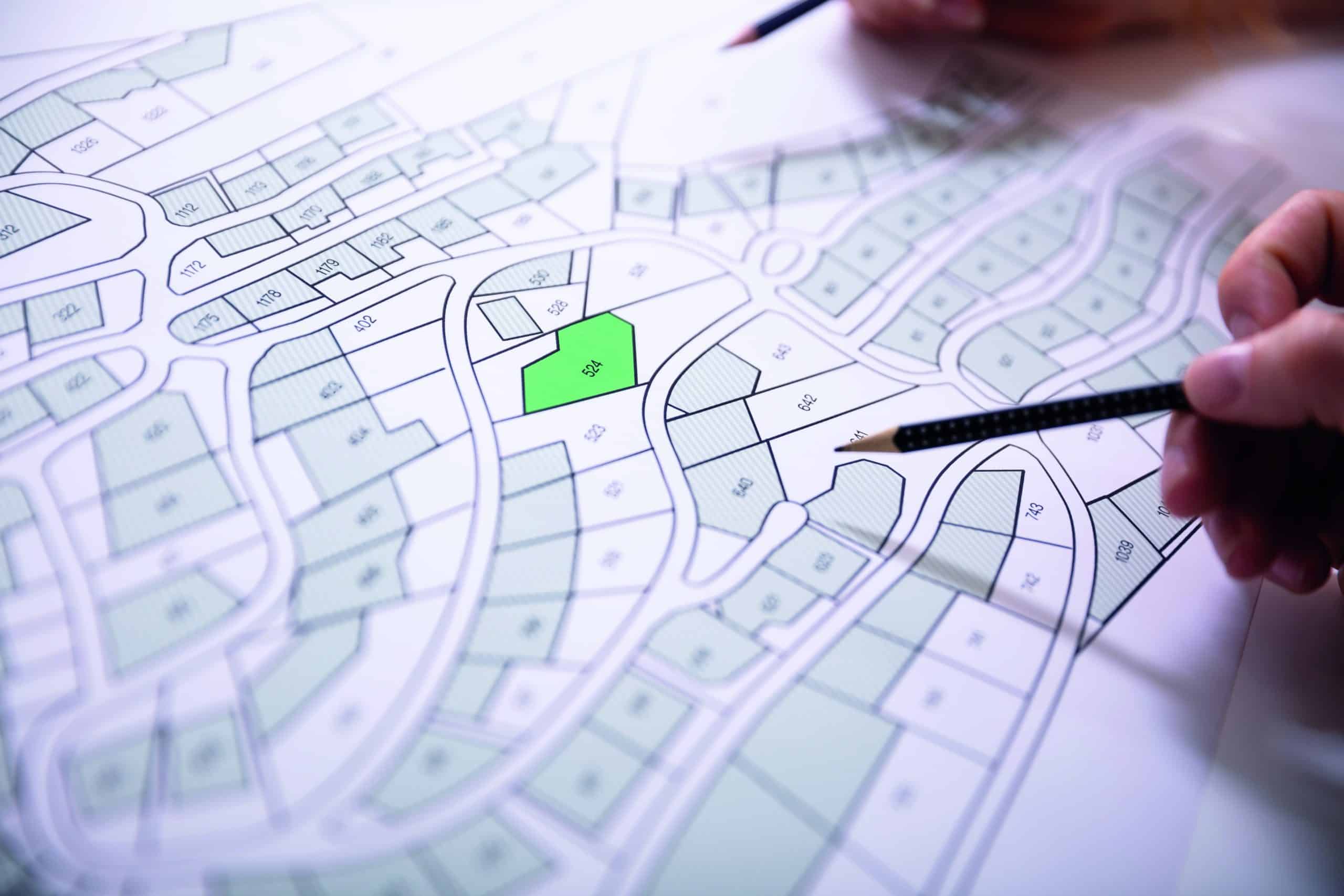 Close-up Of Human Hand Holding Pencil Over Paper Cadastre Map