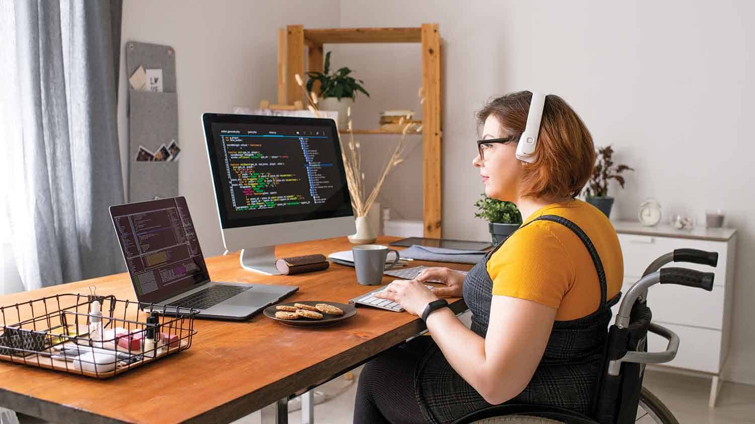 Woman in a wheelchair working on a dual screen computer - coding can be seen.