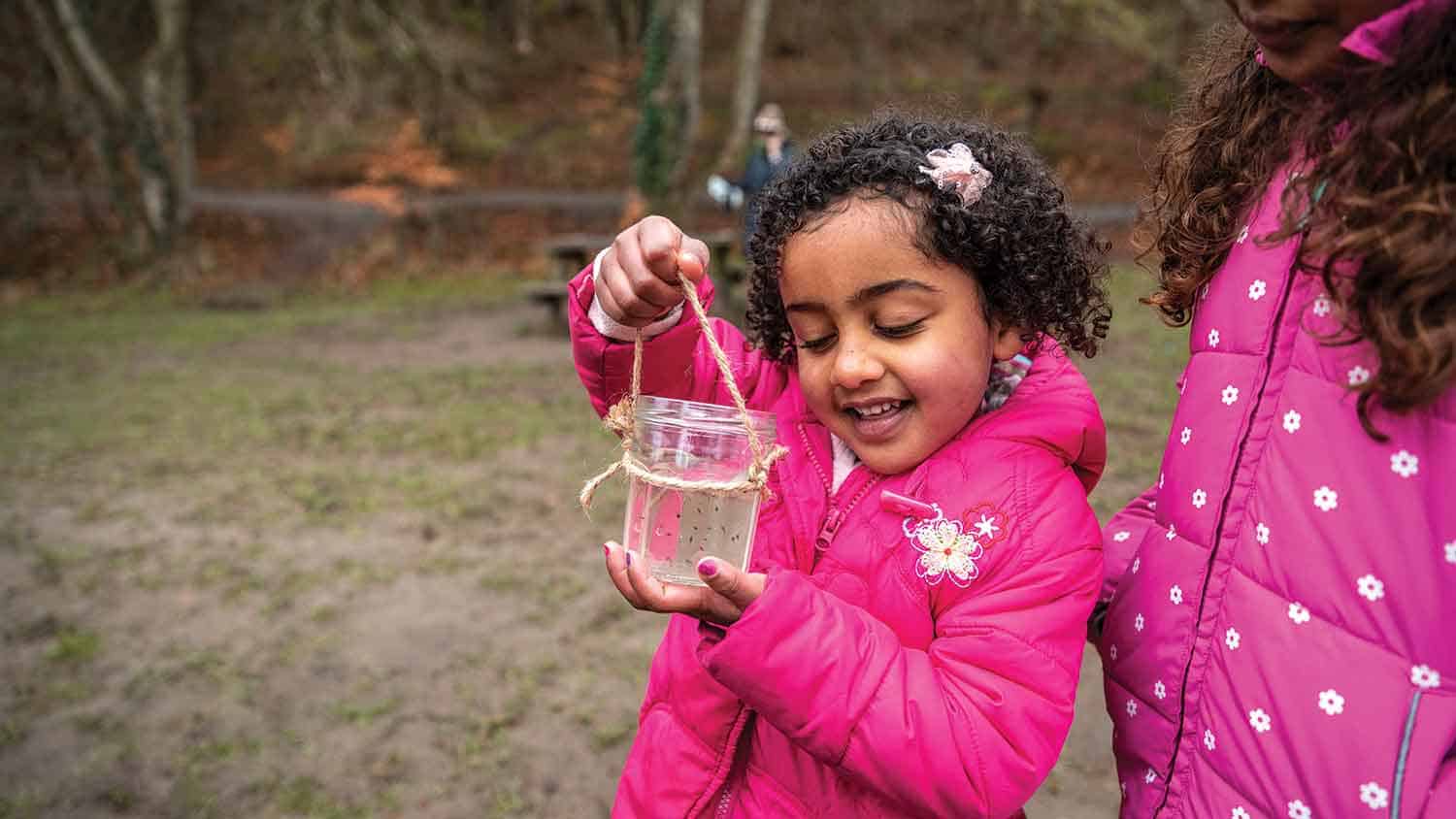 young girl marvelling at something she's caught in a glass beaker in a park.