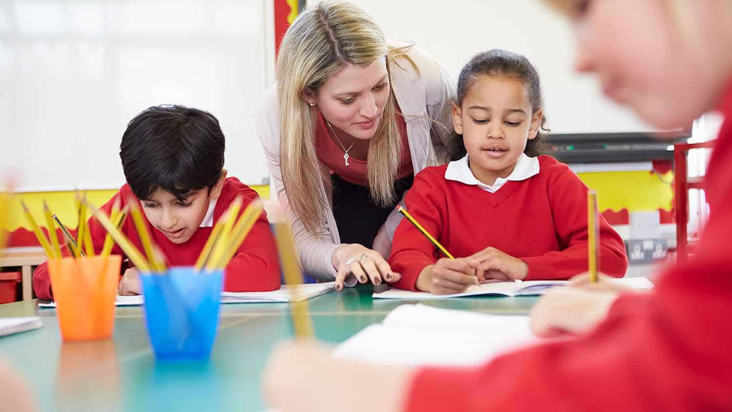 Teacher helping a young pupil (age 5-7) in the classroom.