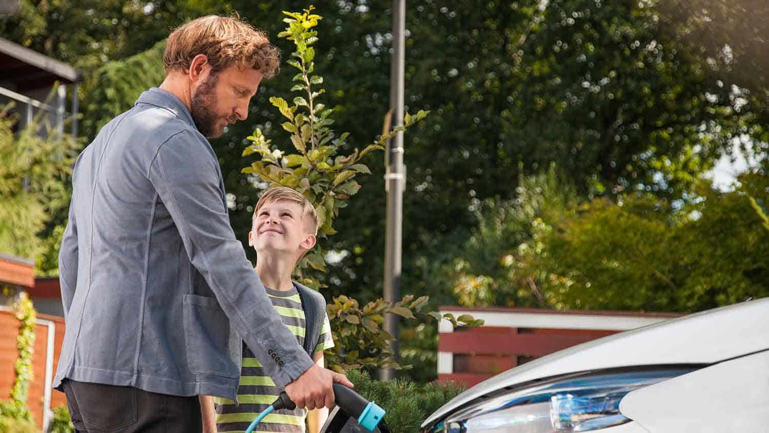 Man connecting the charging lead to a car - his son is next to him smiling