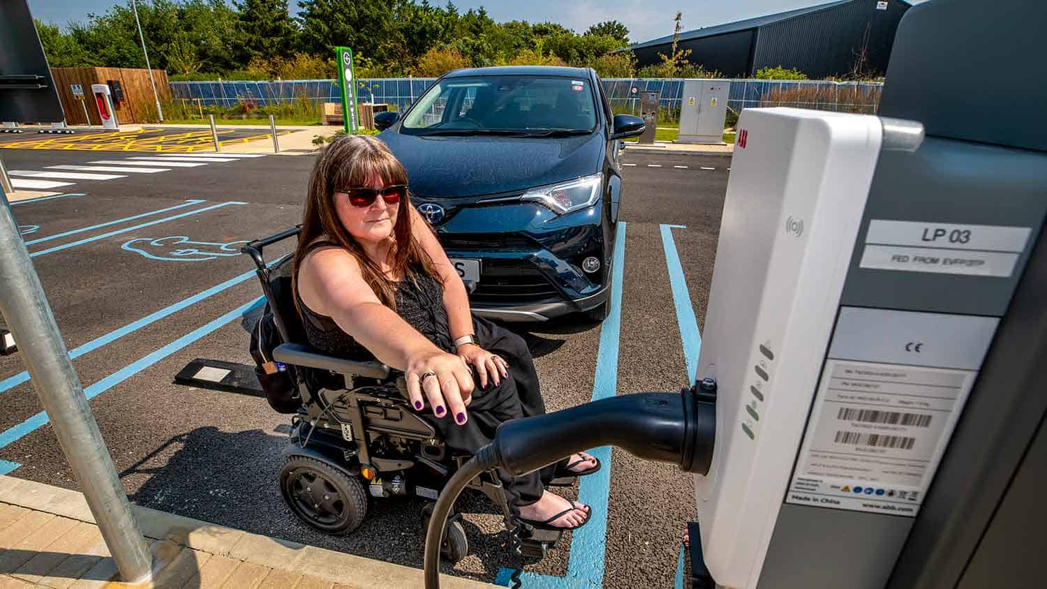 A wheelchair user struggles to reach the electric charge point cable