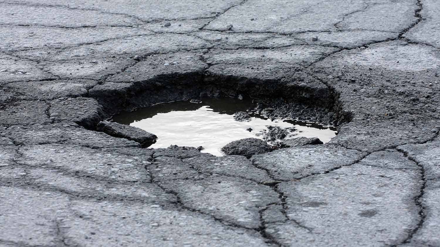 a pot hole in a decrepit road, the hole has some water in it