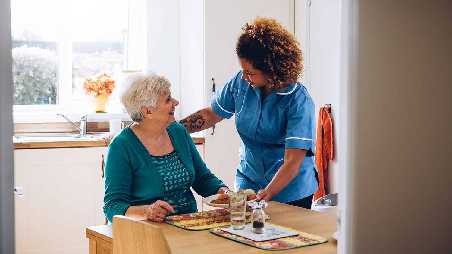 A carer helps an older lady with her meal, they're smiling at each other