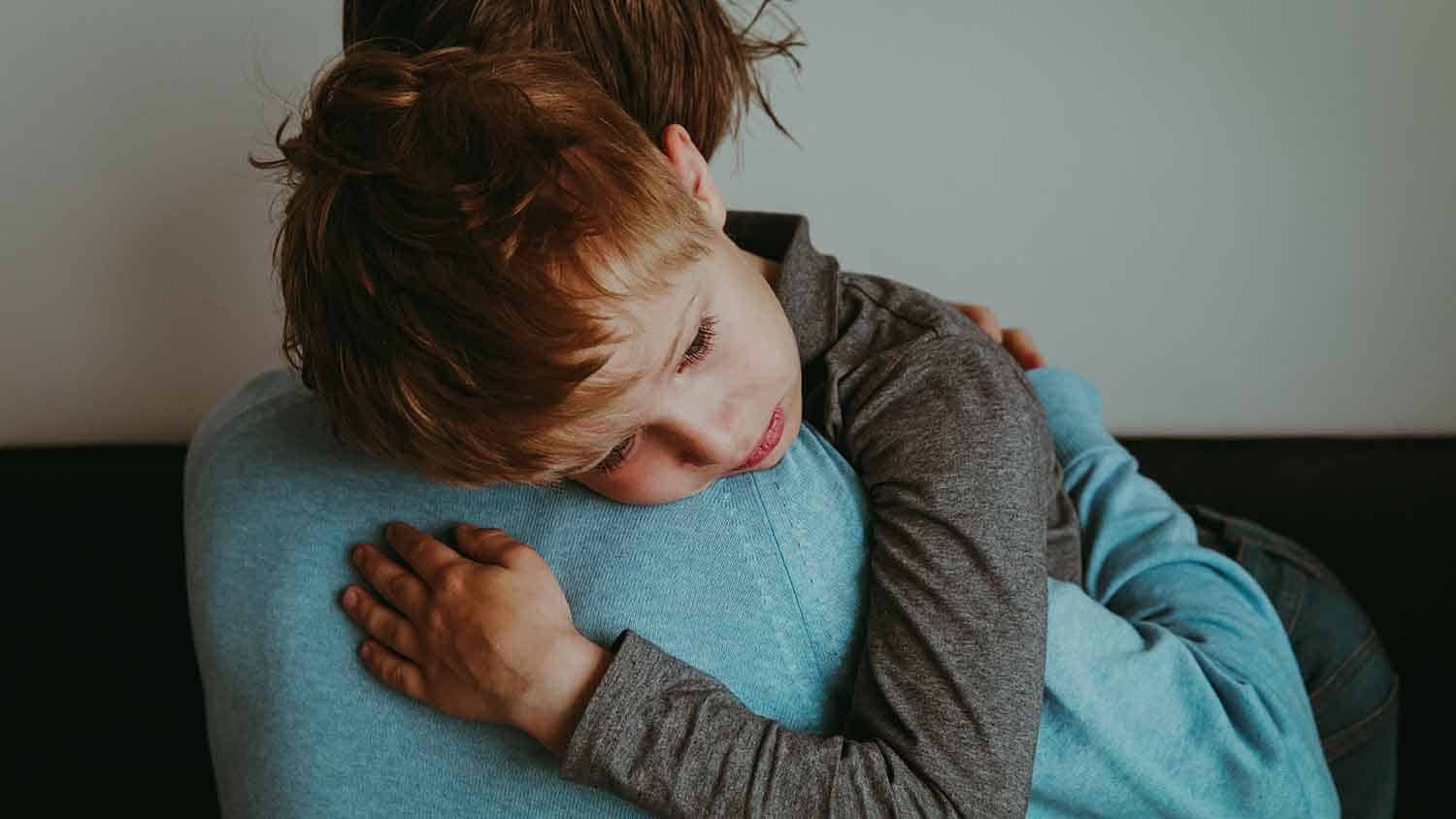 a young boy leans on his mother's shoulders